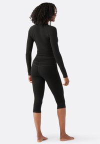 Top negro de manga larga y leggings recortados hechos de tela elástica. Presenta mangas raglán y costuras en contraste. Postura descalzo.