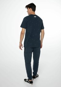 Dunkelblaues Kurzarm-T-Shirt mit kleinen bunten Punkten, kombiniert mit dunkelblauen Jogginghosen mit Seitentaschen und schwarzen Sneakern.