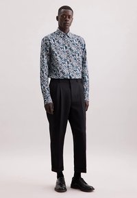 Blauwe bloemetjesblouse met lange mouwen en een overhemdkraag met knopen, gecombineerd met hooggesneden zwarte geplooide broek en zwarte schoenen.