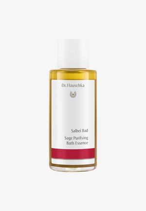 Bouteille en verre transparent contenant un liquide doré, avec un capuchon blanc et une étiquette présentant le nom de la marque, le titre du produit et une bande d'accent rouge.