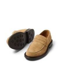 Beżowe mokasyny zamszowe o gładkim wykończeniu, z noskiem typu mokasyn, bocznym przeszyciem oraz czarną, teksturowaną gumową podeszwą z okrągłymi wypustkami.