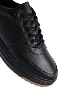 Sneaker in pelle nera con punta arrotondata, chiusura con lacci e collo imbottito. Presenta una superficie testurizzata e suola in gomma con un accento marrone chiaro.