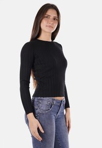 Top lungo a maniche corte nero a coste con colletto rotondo, design aderente e lunghezza corta, abbinato a jeans in denim blu.