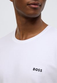 T-shirt bianca in cotone con scollo rotondo e logo "BOSS" ricamato in nero sul lato sinistro del petto. Tessuto morbido.