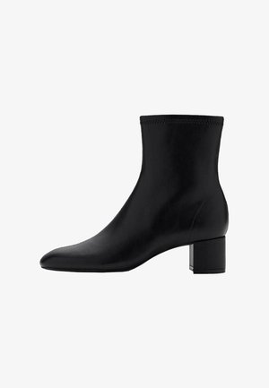 Botín de cuero negro hasta el tobillo con punta afilada y tacón rectangular. Superficie lisa con un sutil detalle de costura alrededor del borde superior.