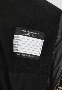 Sort fleece beklædning med en hvid vaskeanvisning, der viser "SWEDEMOUNT" logoet, plads til personlige oplysninger og en bjerggrafik.