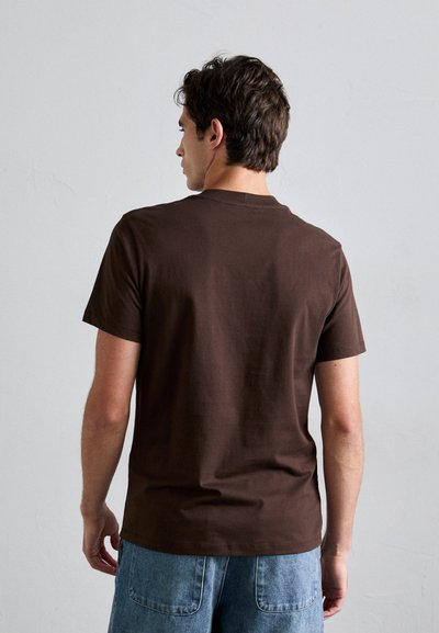 Brun kortermet T-skjorte laget av bomull. Har rund hals og en avslappet passform, kombinert med lyseblå denimshorts.