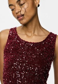 Burgundska bezrukavna majica sa šljokicama, zaobljenog izreza, teksturirane tkanine i blistavog površinskog detalja, koja prikazuje gustu šljokičastu šaru.
