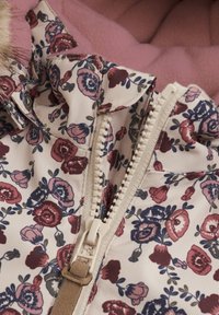 Blommönstrad jacka i ljus krämfärg med rosa fleecefoder, med en central dragkedja och en fuskpälsdetalj på kragen.