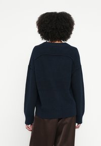 Tengerészkék kötött pulóver texturált felülettel, széles ujjak, bordázott szegéllyel. A hátulja laza szabású, jellegzetes varrásrészletekkel.