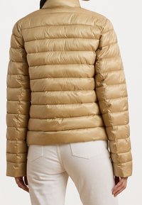 Beige väritetty toppatakki, jossa on tikattu kuvio, korkea kaulus ja sileä pinta. Takissa on pitkät hihat ja vartalonmyötäinen leikkaus.