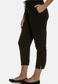 Zwarte cropped broek met een trekkoord in de taille, zijzakken en kleine splitjes aan de onderkant. Zachte stof voor comfort en flexibiliteit.