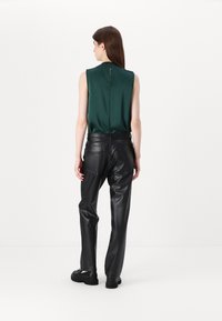 Mouwloze groene satijnen top met een ritssluiting op de rug, gecombineerd met zwarte faux leren broek met zijzakken en een gladde textuur.