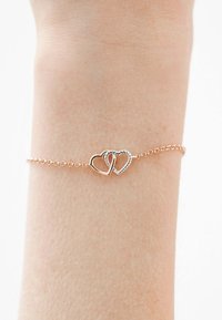 Pulsera de oro rosa que presenta dos corazones entrelazados, uno liso y otro texturizado con un diseño retorcido, montada en una delicada cadena.
