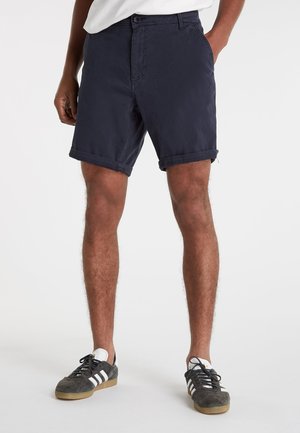 Shorts bleu marine avec un devant plat, ourlet à revers, poches latérales et passants de ceinture ; fabriqués à partir d'un tissu léger en coton.