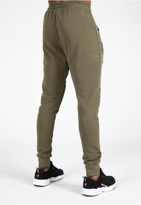 Olijfgroene joggingsbroek met een gestructureerd zijpaneel, elastische tailleband en tapered pasvorm, gecombineerd met zwarte sportschoenen.