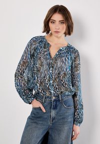 Genomskinlig blus med mönster i blått, grönt och brunt, med knäppning fram och avslappnad passform. Matchas med högmidjade jeans.