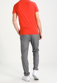 Czerwona koszulka z krótkim rękawem i szare spodnie o fakturowanej powierzchni. Spodnie mają podwinięte nogawki, a osoba ma na sobie białe sneakersy. Widok z tyłu.