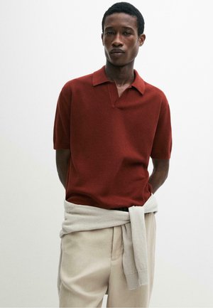 Mann trägt ein rostrot kurzärmeliges Strick-Poloshirt mit einem beigen Pullover um die Taille gebunden und beigen Hosen.