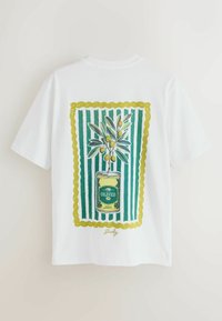 Fehér póló grafikai mintával, amelyen egy olajbogyó ága nő ki egy zöld-sárga színű, olajbogyót ábrázoló dobozból, zöld-fehér csíkos háttér előtt.