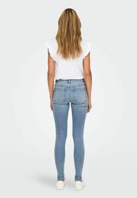 Heledad sinised kitsad teksad kõrge vöökoht, ees ja taga taskud, koos valge volangkäistega topp, kantud valgete tossudega.