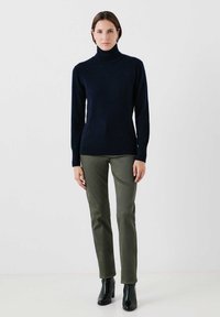 Suéter de cuello alto en azul marino hecho de material suave, combinado con pantalones de color verde oliva y botas negras de tobillo. Diseño simple y ajustado, con mangas largas.