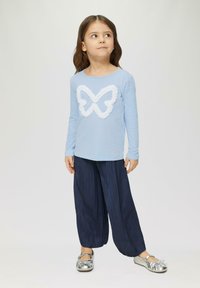 Lichtblauw shirt met lange mouwen met een textuurontwerp van een witte vlinder, gecombineerd met marineblauwe geplooide wijde broek en zilveren ballerina's.