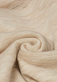Beige Strickstoff mit weicher Textur, präsentiert in einer gefalteten und verdrehten Anordnung, mit subtilen Streifen und feinem Gewebe.