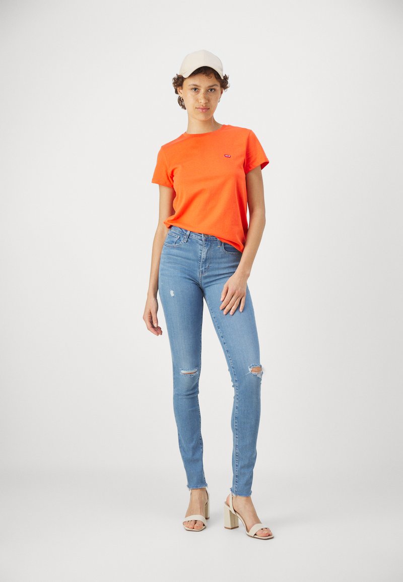 Helles oranges Baumwoll-T-Shirt mit Rundhalsausschnitt und kurzen Ärmeln, kombiniert mit hellblauen Skinny-Jeans mit Kniefen und hohen Schuhen.