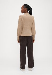 Maglione a maglia beige con collo alto e polsini a costine, abbinato a pantaloni in velluto a coste marrone scuro a gamba larga e scarpe da ginnastica bianche.