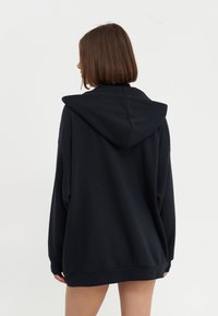 Crna oversized kapuljača napravljena od mekanog materijala, s kapuljačom na vezanje, dugim rukavima i rebrastim rubom. Minimalistički dizajn bez vidljivih logotipa.