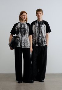 Μπλούζες με κοντά μανίκια σε μαύρο και άσπρο με αφηρημένο σχέδιο και μαύρα μανίκια, σε συνδυασμό με φαρδιά μαύρα παντελόνια. Το κείμενο στη μπλούζα αναγράφει "Coel."