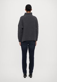 Szary sweter prążkowany z wysokim kołnierzem i rękawami w warkoczyki, zestawiony z ciemnoniebieskimi dżinsami. Stylizacja dopełniają eleganckie czarne buty.