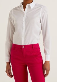 Camisa blanca de manga larga con botón y cuello clásico, combinada con pantalones ajustados rosa brillante que cuentan con un bolsillo frontal y cierre de botón.