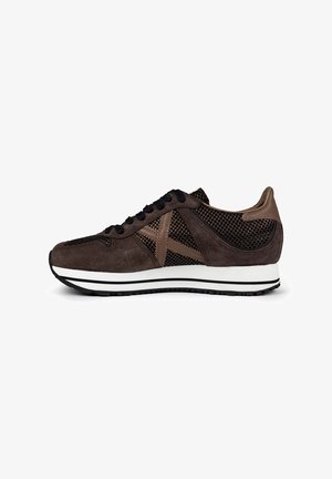 Zapatillas de ante marrón con acentos de malla, cordones negros, entresuela blanca con detalle de rayas negras y diseño de puntera redondeada.