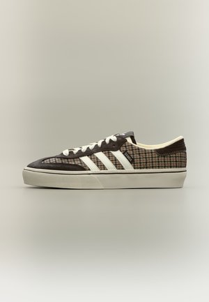 Niski sneaker z wzorem w jodełkę i ciemnymi panelami z zamszu, białymi sznurowadłami, trzema białymi paskami i kremową gumową podeszwą.