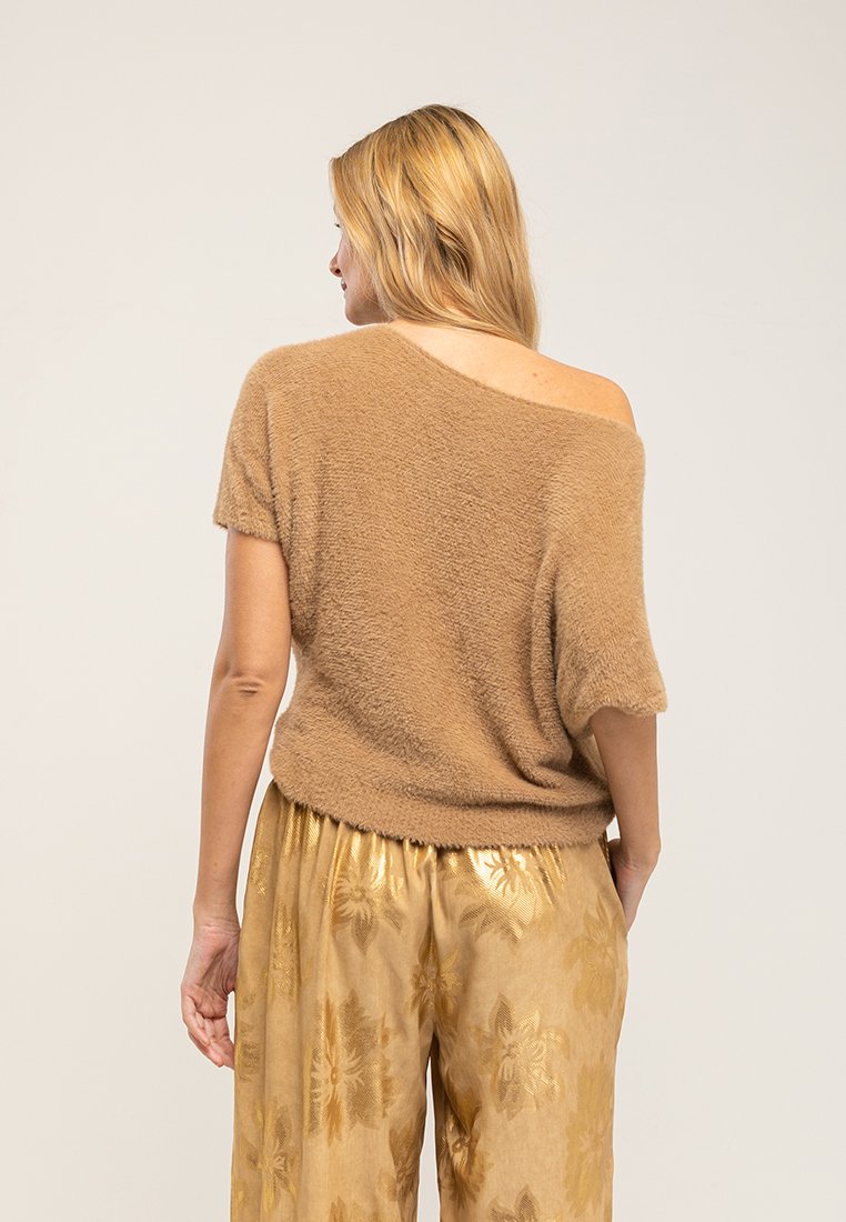 Brązowy, puszysty sweter z dekoltem na jednym ramieniu, w połączeniu ze złotymi satynowymi spodniami w kwiatowy wzór. Miękka tekstura i luźny krój.