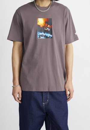 Camiseta de algodón gris con un estampado gráfico central en colores vibrantes. Mangas cortas y un corte relajado, combinada con pantalones de mezclilla azul.
