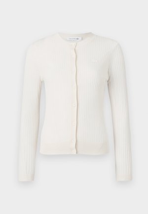 White ribbed cardigan with long sleeves, round neckline, and front buttons. Features a small logo on the chest. Soft texture.