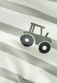 Graphique de tracteur vert et noir sur un tissu doux à rayures horizontales gris et blanc, gros plan montrant la texture et les détails.