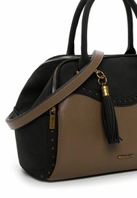 Zwarte en bruine handtas van gestructureerd synthetisch leer, met een ritssluiting, decoratieve perforaties en een kwastaccent aan de schouderriem.