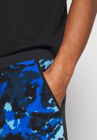 Camisa de algodón negra con bolsillo que presenta un vibrante patrón abstracto en azul y negro sobre un tejido de forro polar, resaltando la textura y el contraste de color.