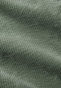 Groen corduroy stof met verticale ribbels en een zachte textuur. Het materiaal lijkt pluche en heeft een rijke, consistente kleur.