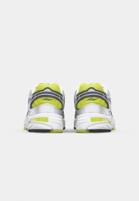 White and gray athletic shoes with green accents, featuring a textured mesh upper and sturdy rubber sole, visible branding on the heel.