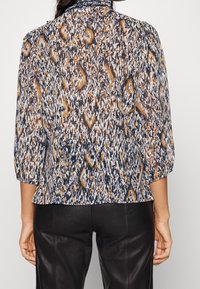 Blusa a fantasia floreale in blu navy, arancione e crema, con maniche a tre quarti, texture plissettata e collo alto. Si ferma sui fianchi.