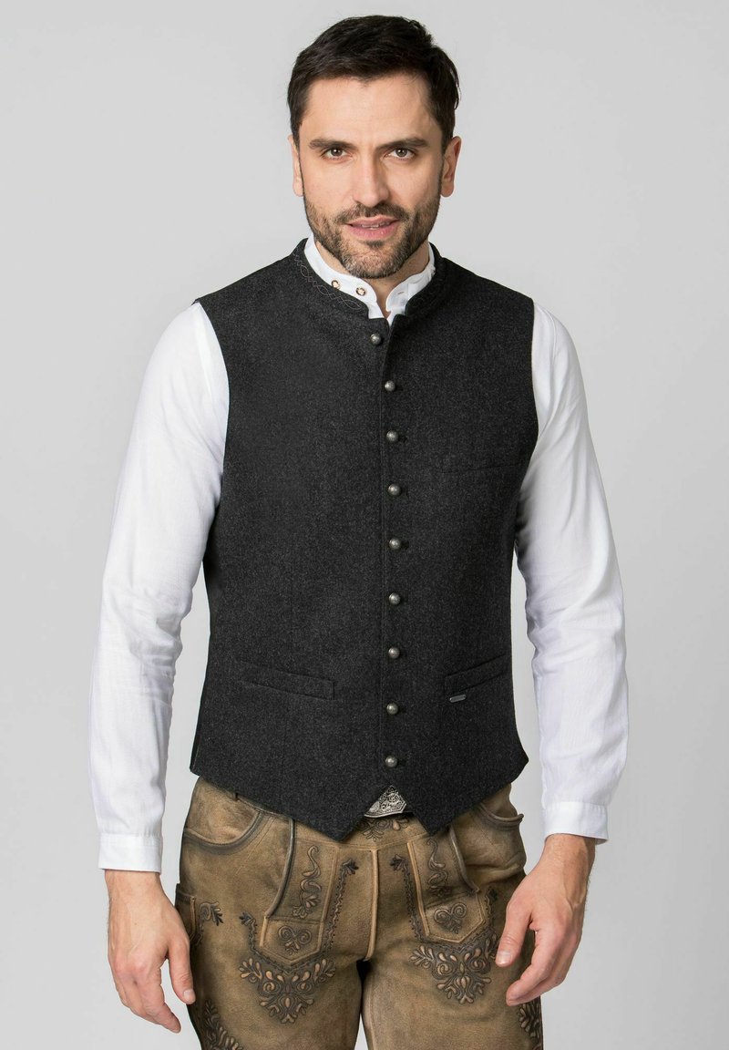 Graue Wollweste mit hohem Kragen, vorderem Knopfverschluss und zwei Taschen. Über einem weißen Hemd getragen, kombiniert mit traditionellen braunen Lederhosen.