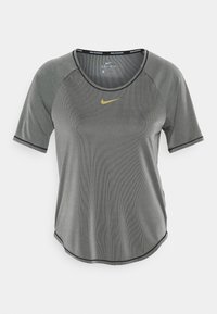 Šedé sportovní tričko s kulatým výstřihem, krátkými rukávy, texturovanou tkaninou a černým prošitím. Na hrudi má malé žluté logo Nike.