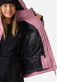 Pink isoleret jakke med sort inderside. Funktioner inkluderer et vandtæt mærke, netlomme og forstærket syning langs sømmene.