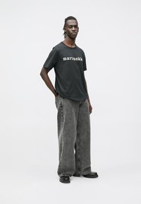 Μαύρο βαμβακερό T-shirt με το λογότυπο "marimekko", συνδυασμένο με φαρδιά, ξεθωριασμένα γκρίζα τζιν. Η εμφάνιση έχει άνετη εφαρμογή και υφή υφάσματος.