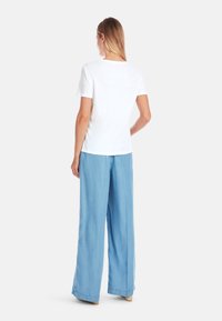 White short-sleeve t-shirt with a round neck, paired with light blue wide-leg pants, showing a relaxed fit and soft fabric texture.